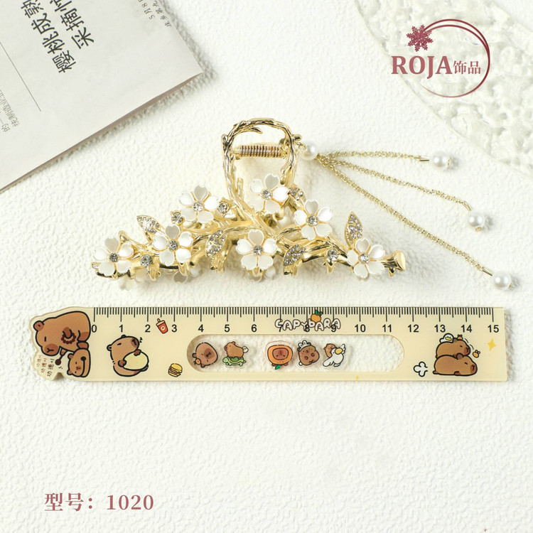 کلیپس موی زنانه فلزی طلایی طرح شکوفه، قرارگرفته کنار خطکش برای نمایش دقیق ابعاد واقعی محصول وارداتیح